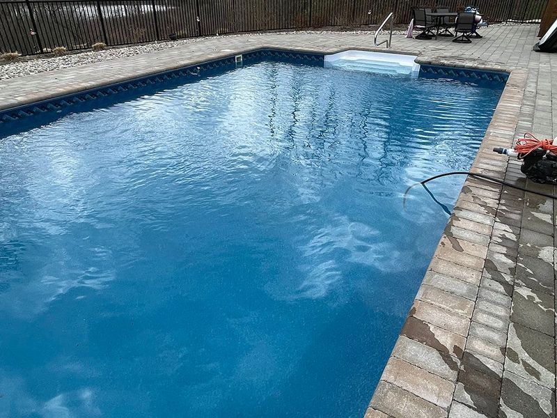 A rectangular pool with clear blue water and a built-in jacuzzi, surrounded by brick pavers.
