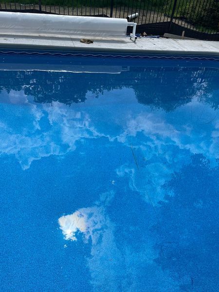 Blue swimming pool reflecting a bright sky with clouds.