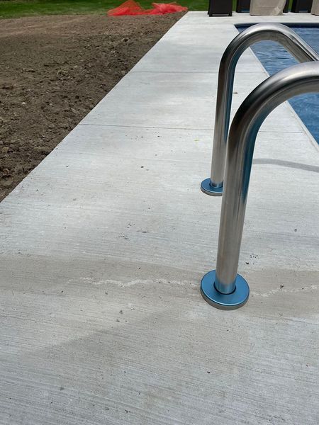 Stainless steel pool ladder on a concrete pool deck.
