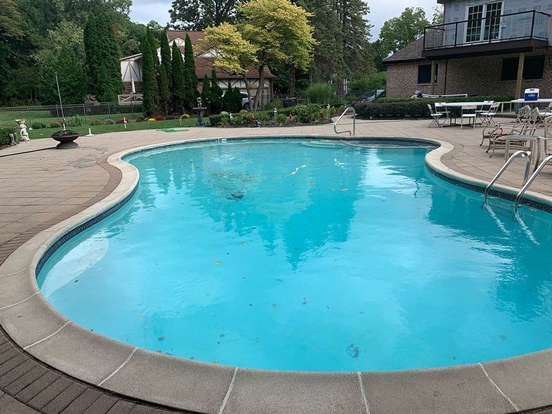 Swimming pool with blue water and surrounding stone patio on a sunny day.