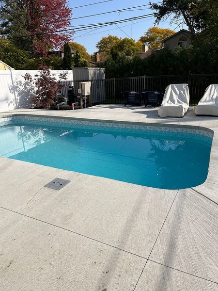 Backyard pool with light blue water and concrete deck; two white covered lounge chairs.