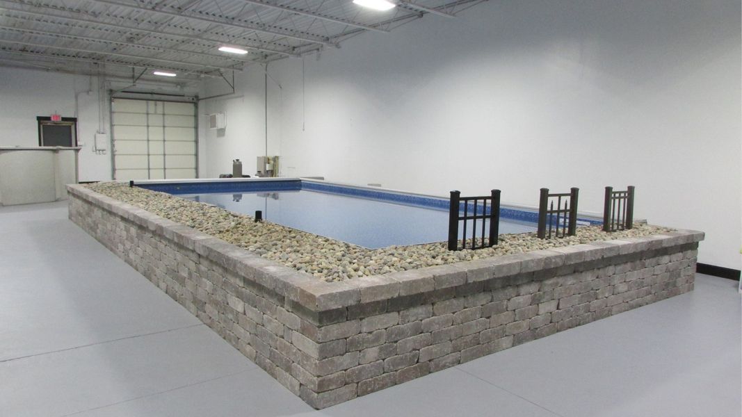Indoor rectangular pool with a stone wall surround, in a white-walled room, with a closed overhead door.