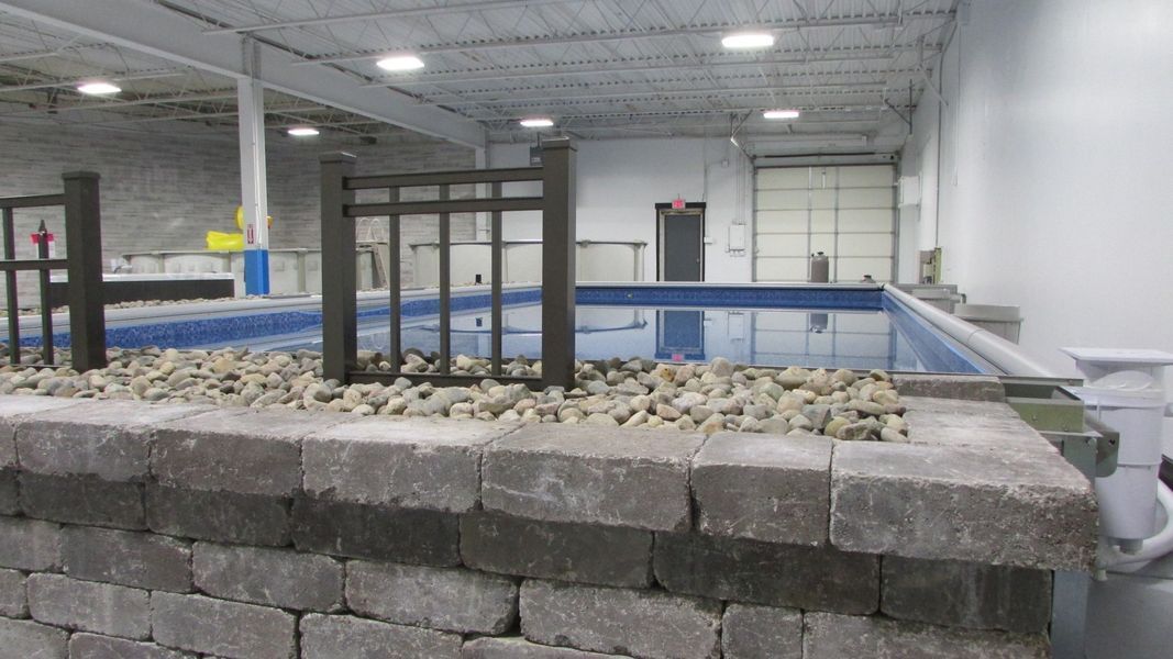 Indoor swimming pool with decorative stone wall, gravel, and small fence in front. White walls, garage door visible.