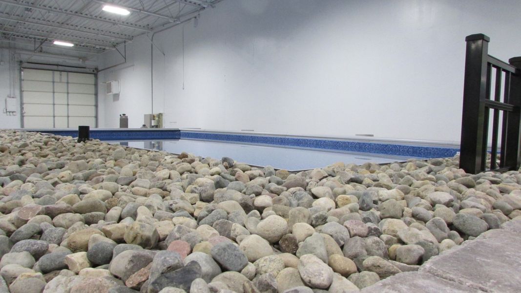 Indoor swimming pool with stone perimeter. Bright, white walls and a garage door in the background.