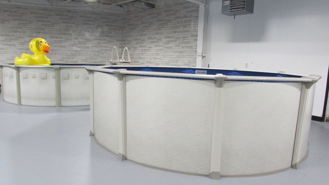 Two above-ground pools, one with a yellow rubber duck, in a room with a white wall and floor.