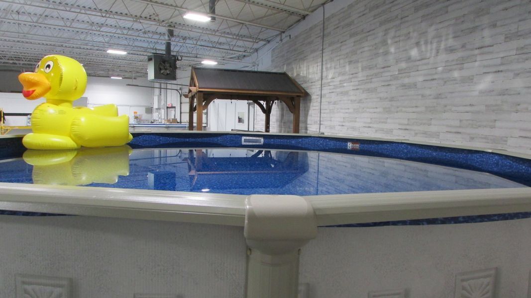Large yellow inflatable duck floating in an indoor pool with a small wooden gazebo in the background.