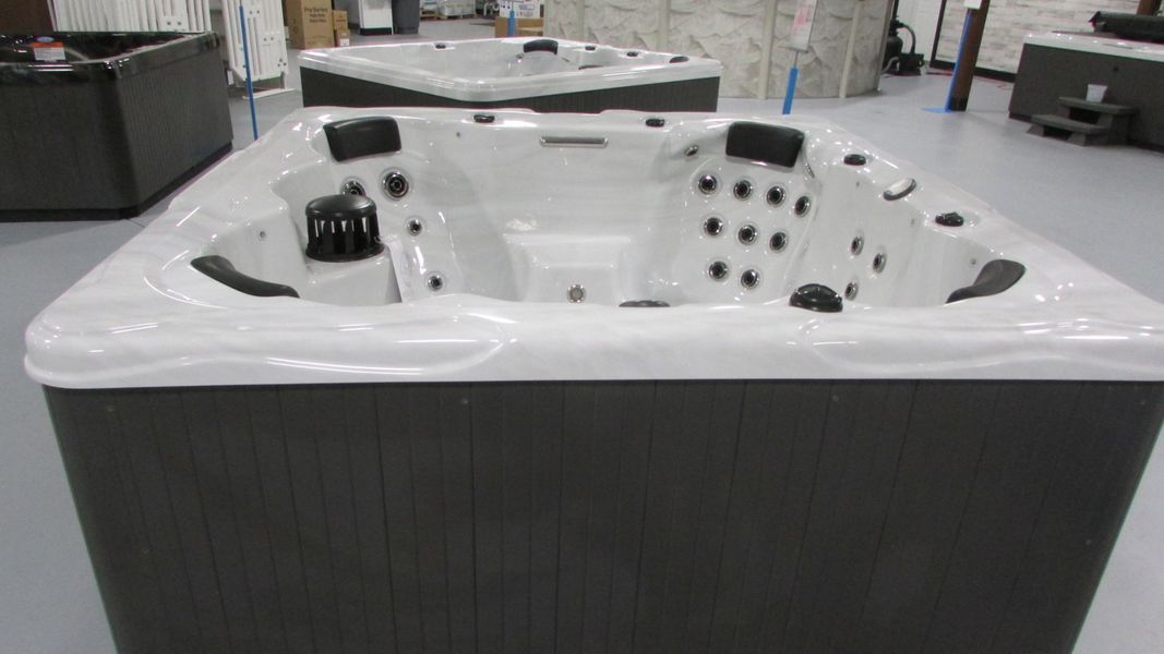 Several hot tubs displayed in a showroom. They have dark grey siding and light interiors.