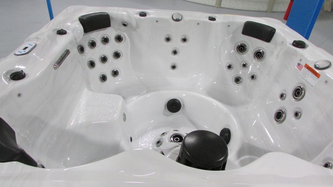 White hot tub with multiple jets and black headrests, indoors.