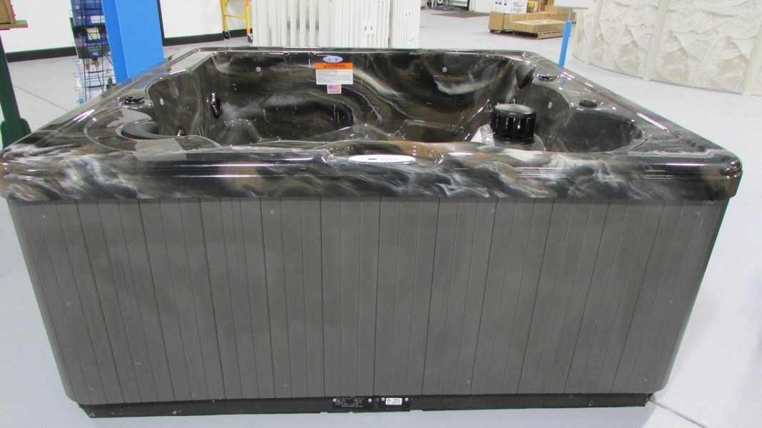 A rectangular hot tub with dark gray siding and a marble-patterned interior, viewed indoors.