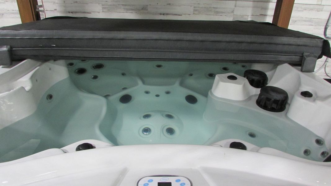 A hot tub with water and jets, cover is open, indoors.