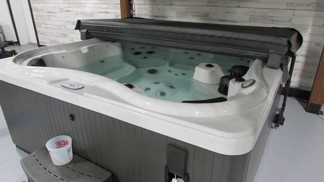 Hot tub with water and partially open black cover in a white and gray room.