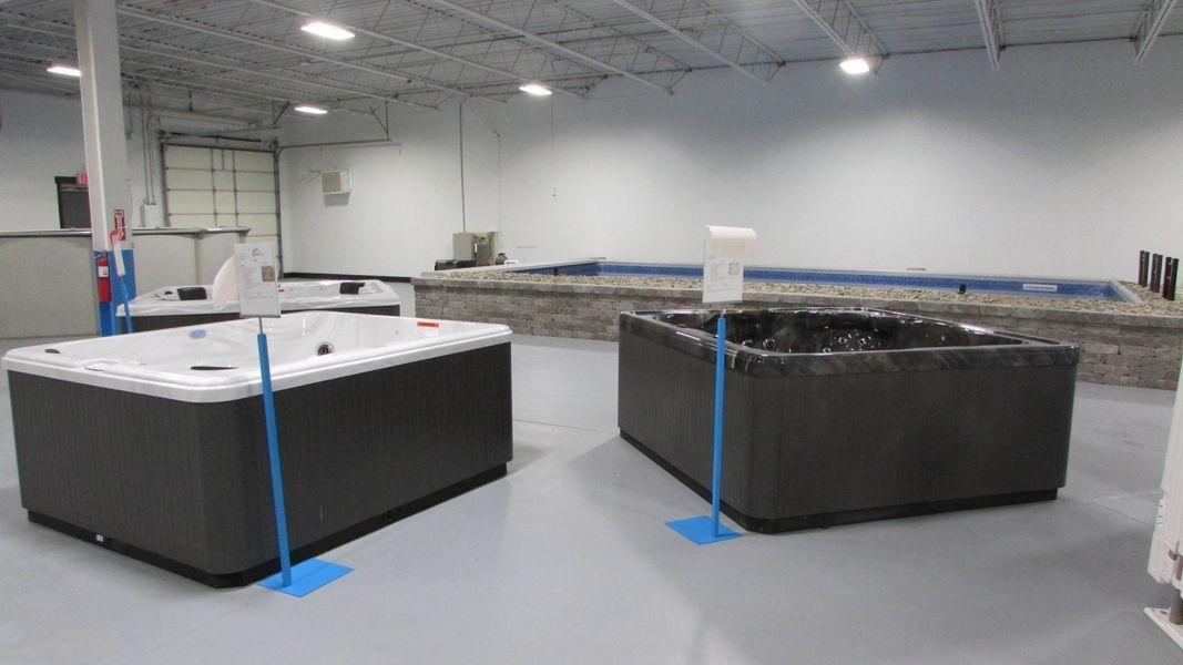 Two hot tubs on display in a showroom, white and black. Grey floor and walls.