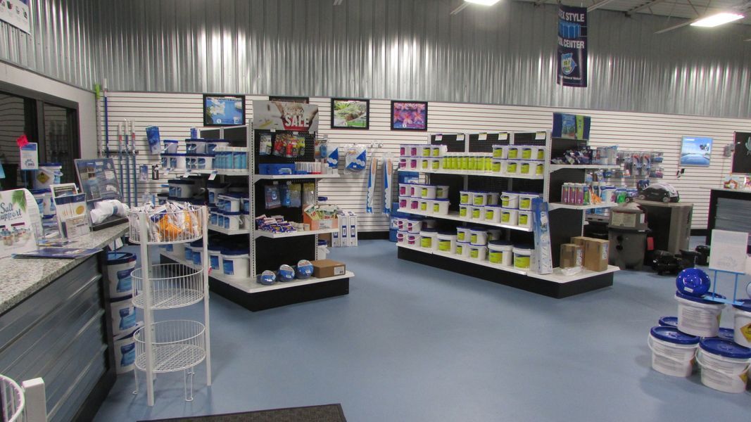 Inside a store, shelves stocked with pool supplies; blue floor, white walls and corrugated metal ceiling.
