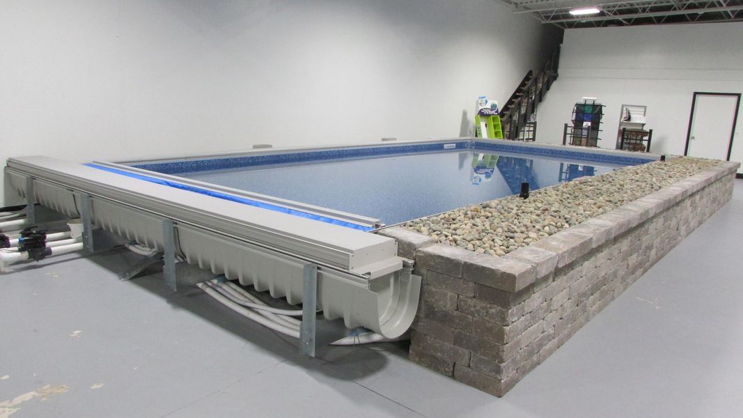 Above-ground rectangular pool with a stone wall and retractable cover.
