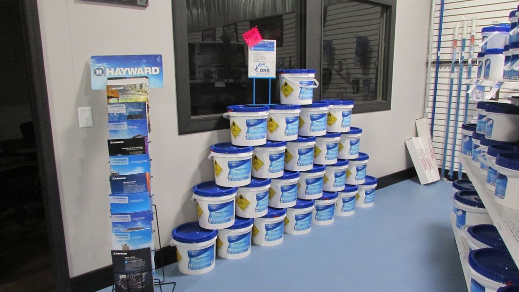 Display of blue and white chemical buckets, likely for pool maintenance, stacked in a store.