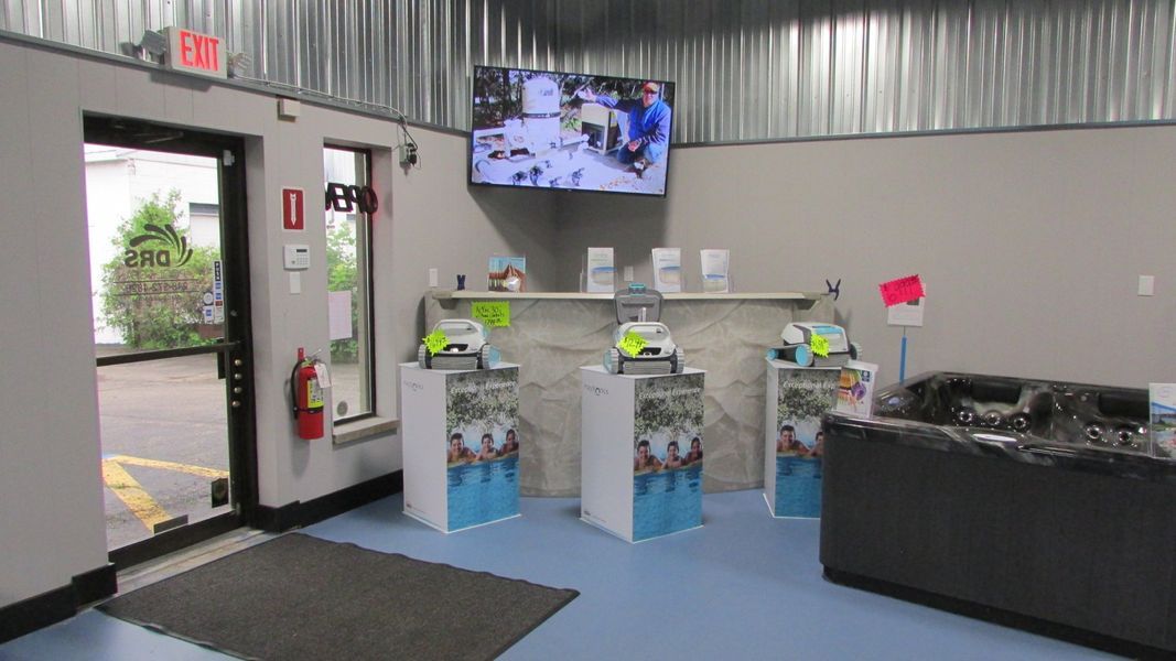 Interior of a shop with a blue floor, displays, and a TV; a doorway leads to outside.
