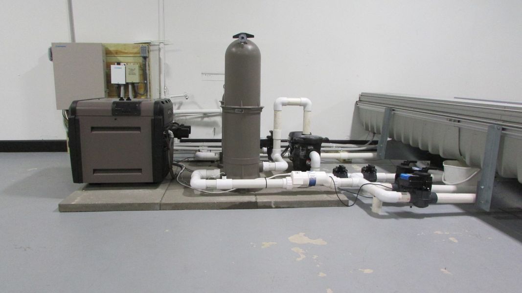 Pool equipment room with pipes, filter, pump, heater, and rectangular tanks.