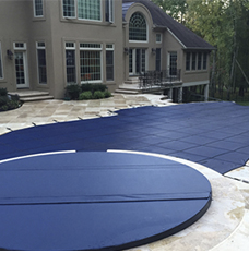 Blue pool cover over a backyard pool, with a large house in the background.