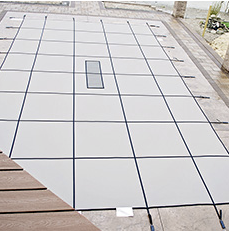 White pool cover stretched over a rectangular pool, secured by straps.