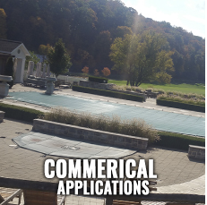 Pool area with a closed pool cover, stone patio, and hillside in the background. 