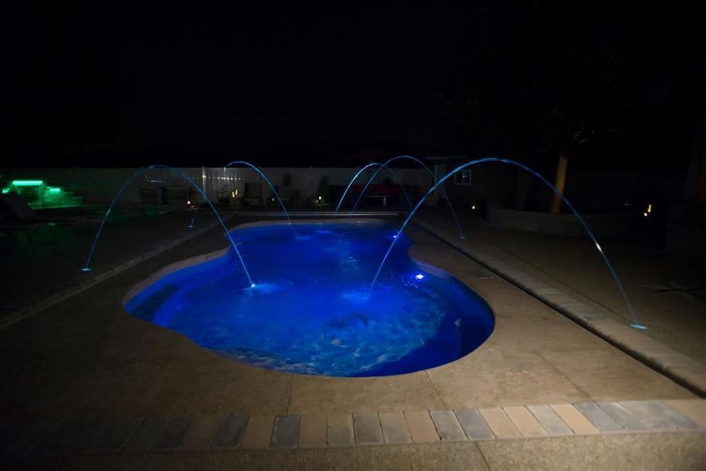 Pool at night with blue lights and water fountains. Dark setting.