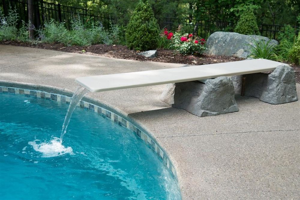 Swimming pool with a diving board made of a stone slab and supports; water pours from the pool edge.