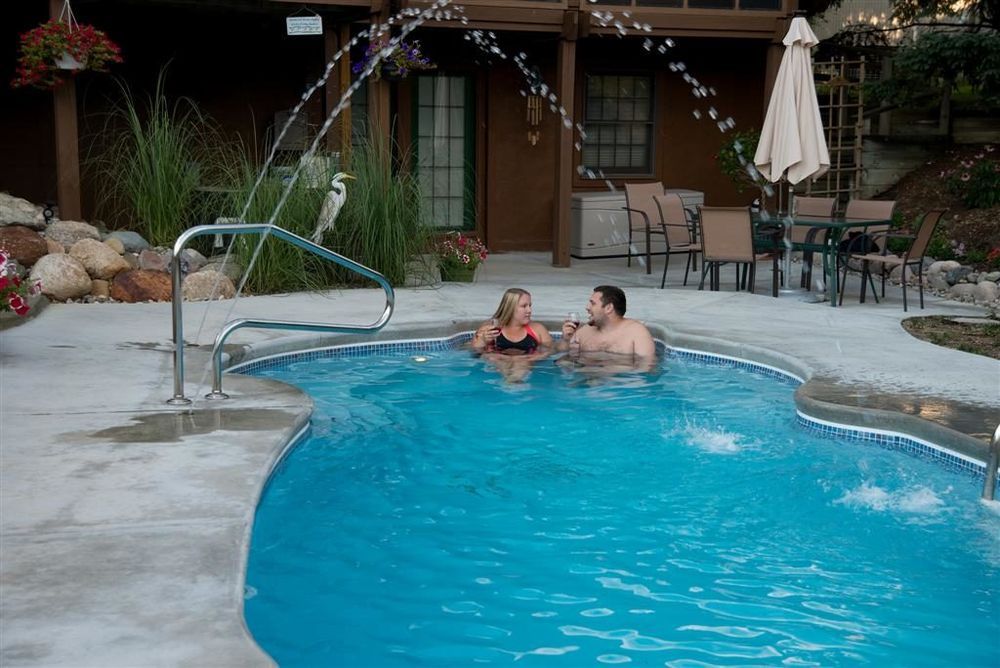 Couple in pool with fountain. Outdoor setting with patio furniture and brown building.