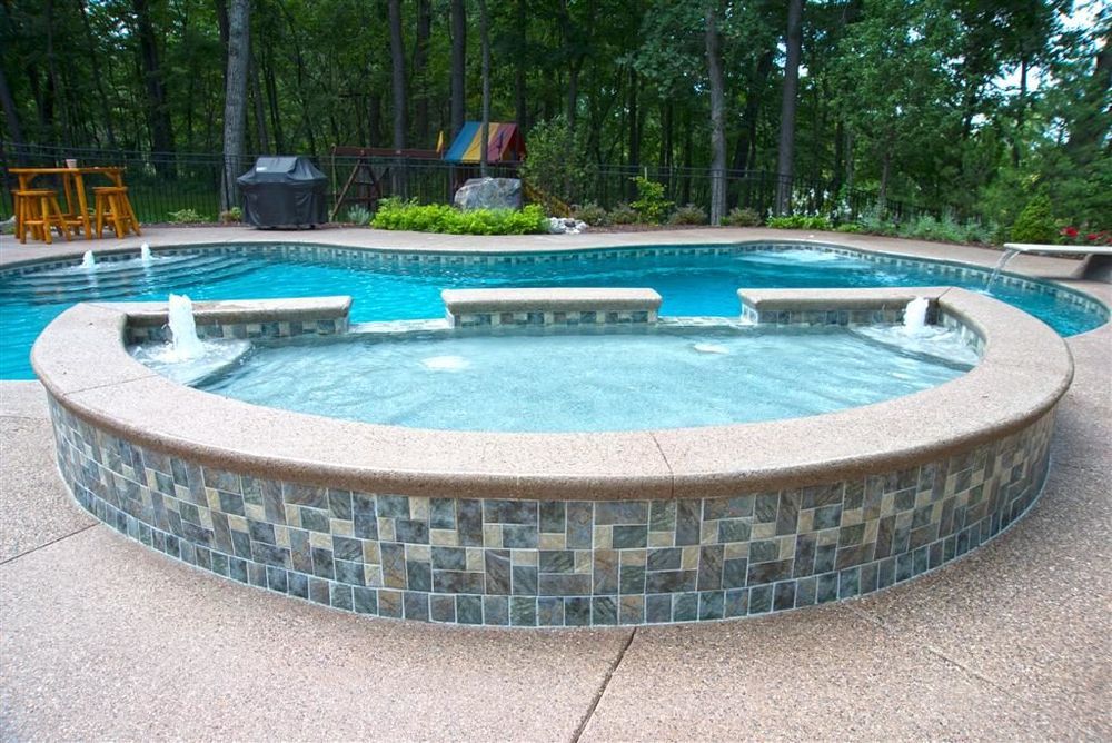 A curved in-ground pool with a raised spa, tiled with blue-green mosaic, and fountains.