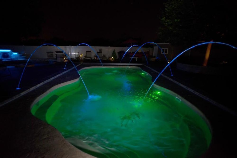 Night view of a glowing green pool with blue fountain jets, against a dark sky.