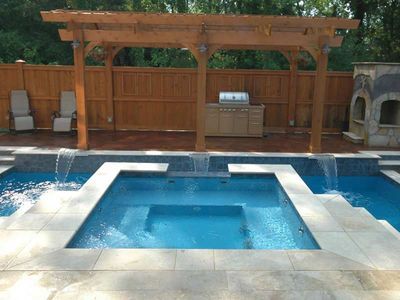 Backyard with pool and spa, waterfall features, wooden pergola, outdoor kitchen, and stone fireplace.