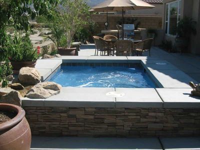 Hot tub surrounded by stone and concrete patio, with patio furniture and umbrella in background.