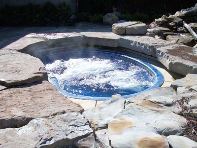 Bubbling hot tub surrounded by large rocks and stone patio. Steam rises.