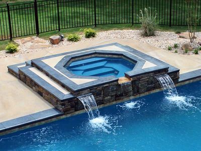 Pool with a built-in spa; water cascades from the spa into the pool. Dark stone accents, blue water.
