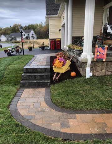 A wheelbarrow filled with flowers and pumpkins is in front of a house.