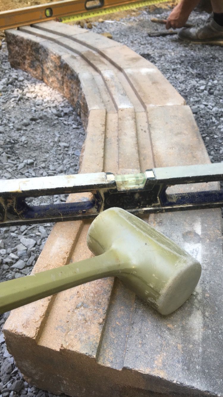 A green hammer is sitting on top of a brick block next to a level.