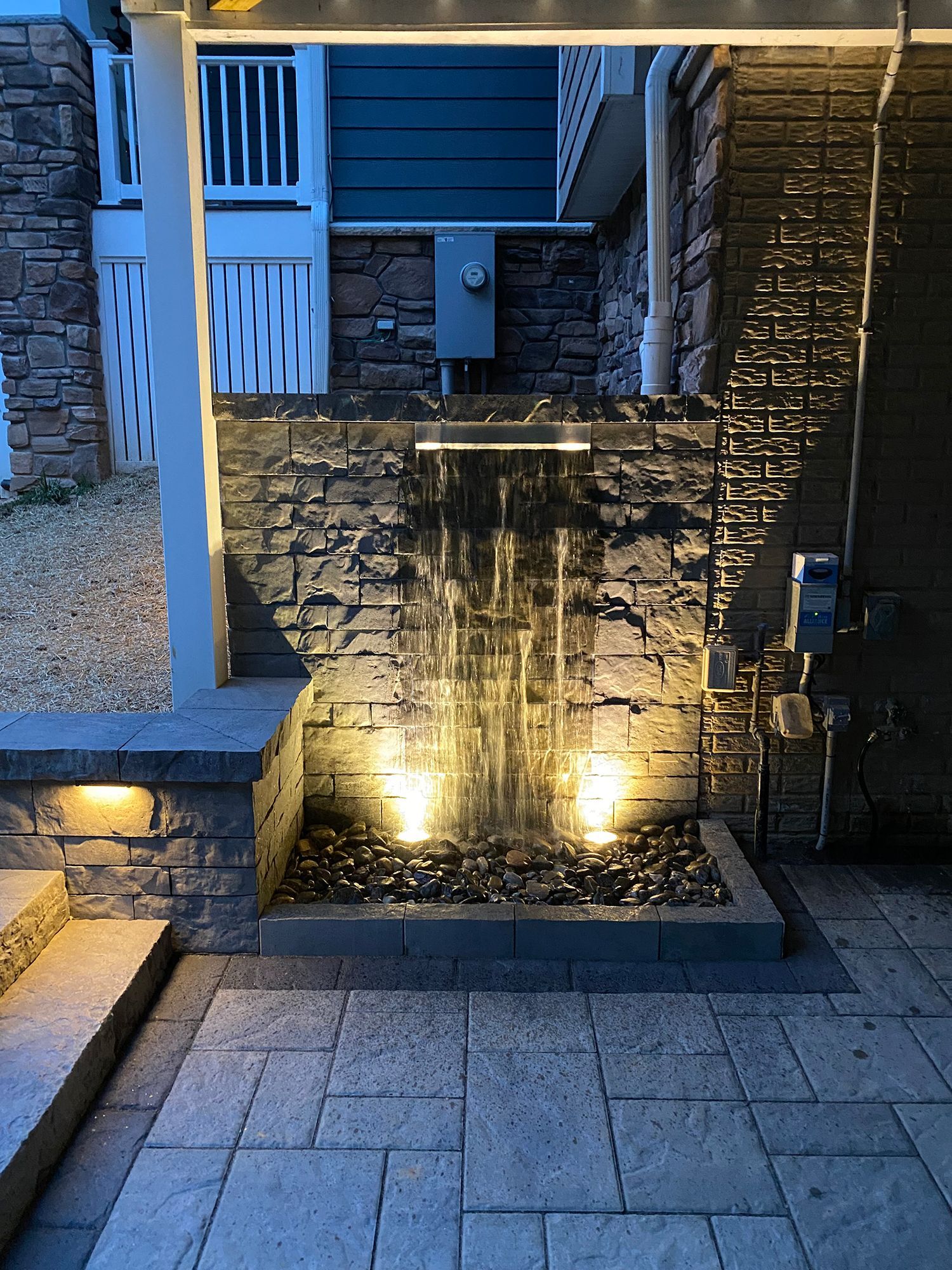 A waterfall is surrounded by bricks and is lit up at night.