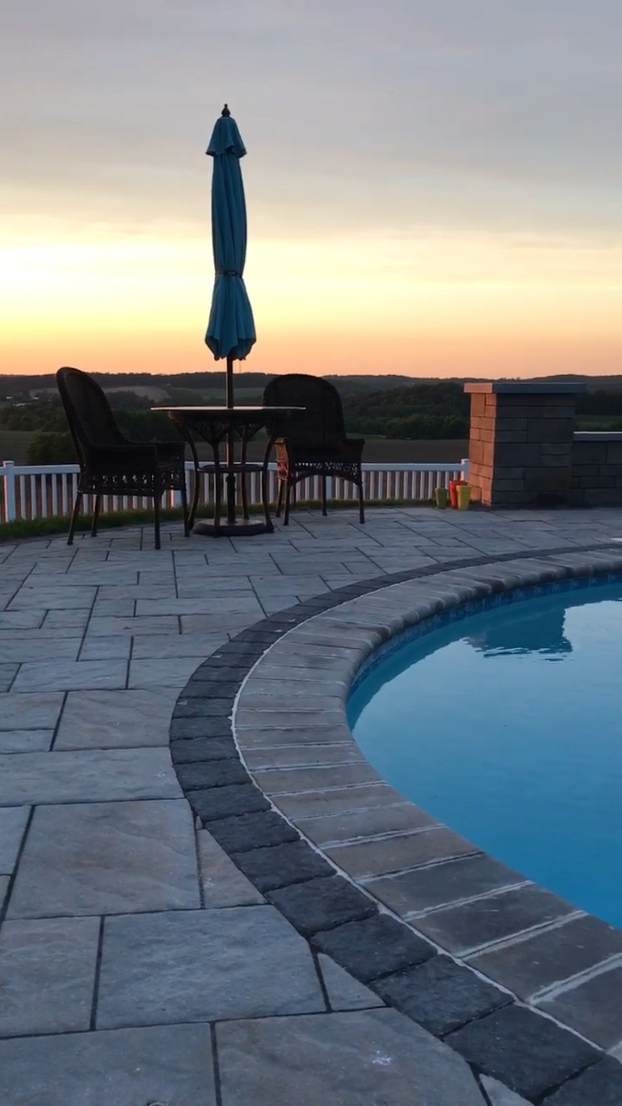 A swimming pool with a table and chairs and a blue umbrella
