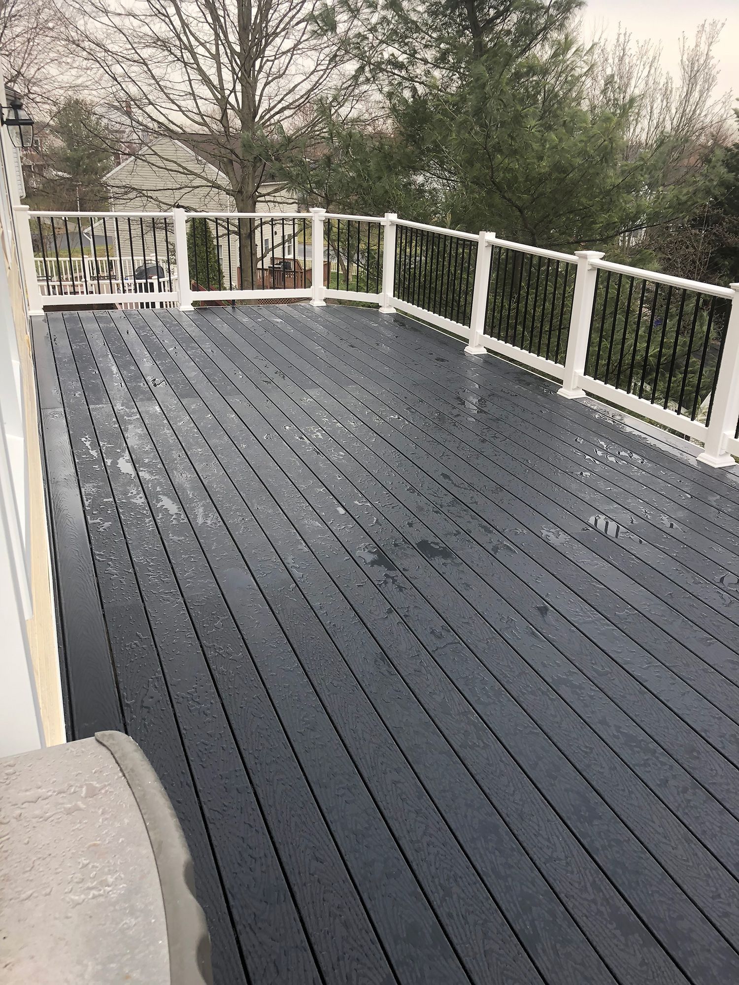 A black deck with a white railing and trees in the background.