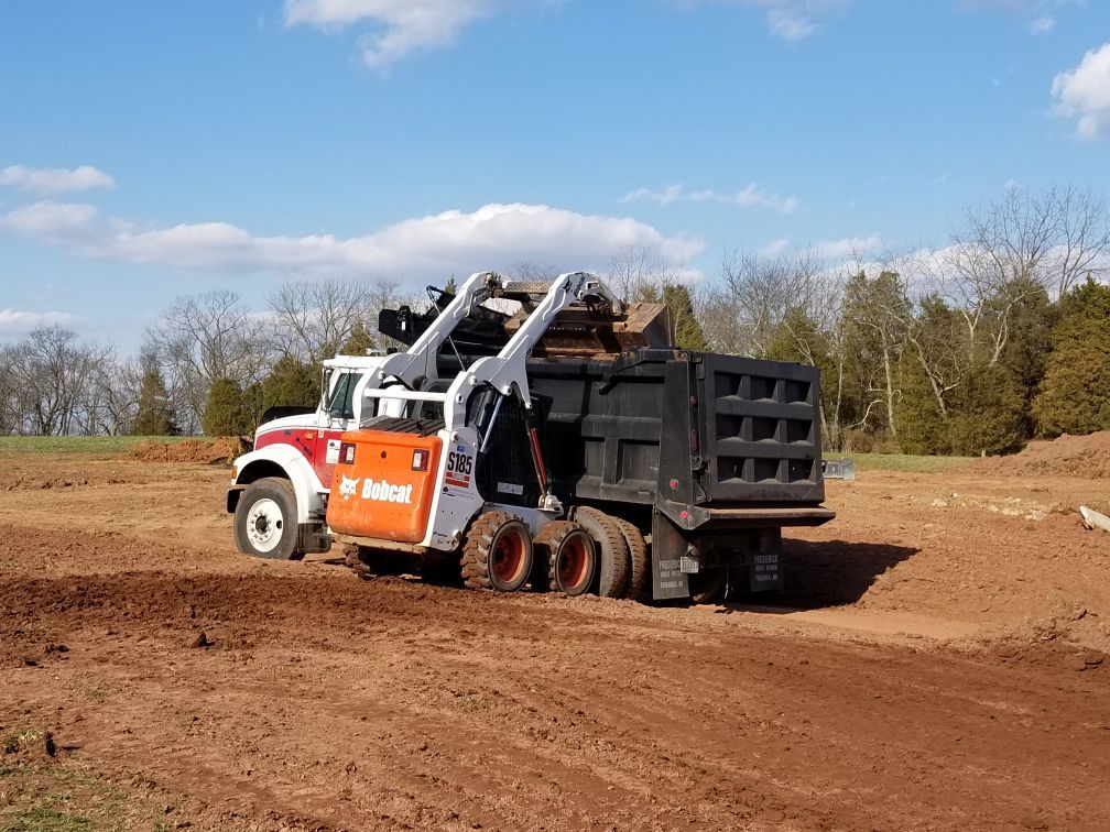 A bobcat dump truck is driving through a dirt field.