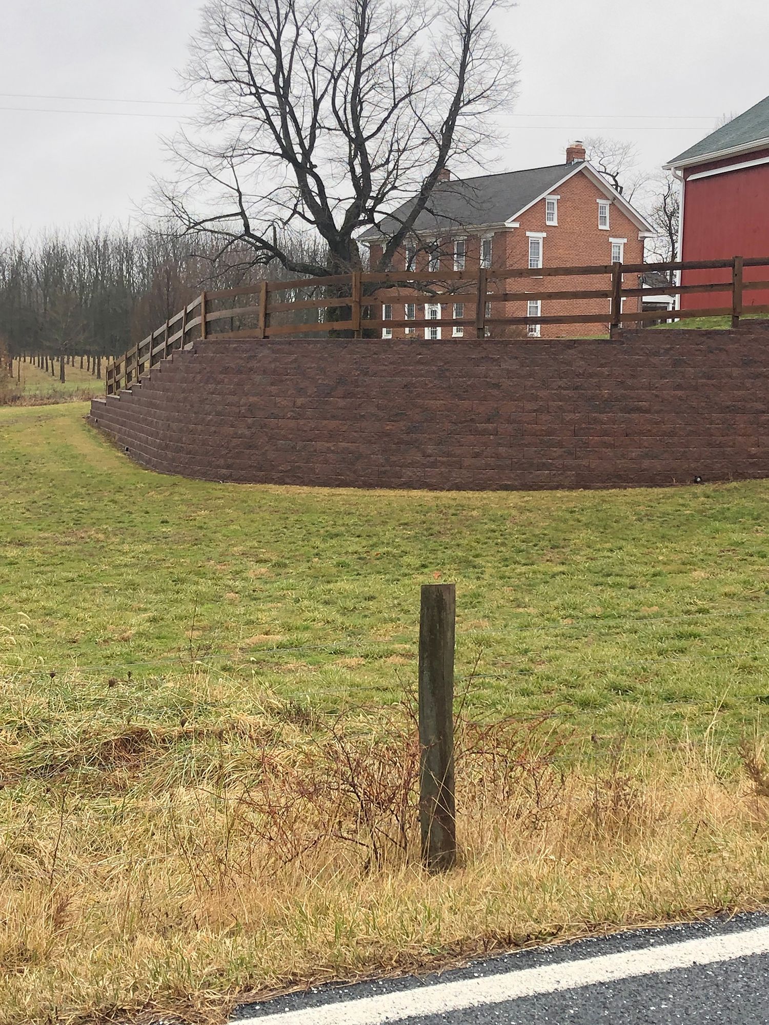 A wooden fence surrounds a grassy field with a red barn in the background.