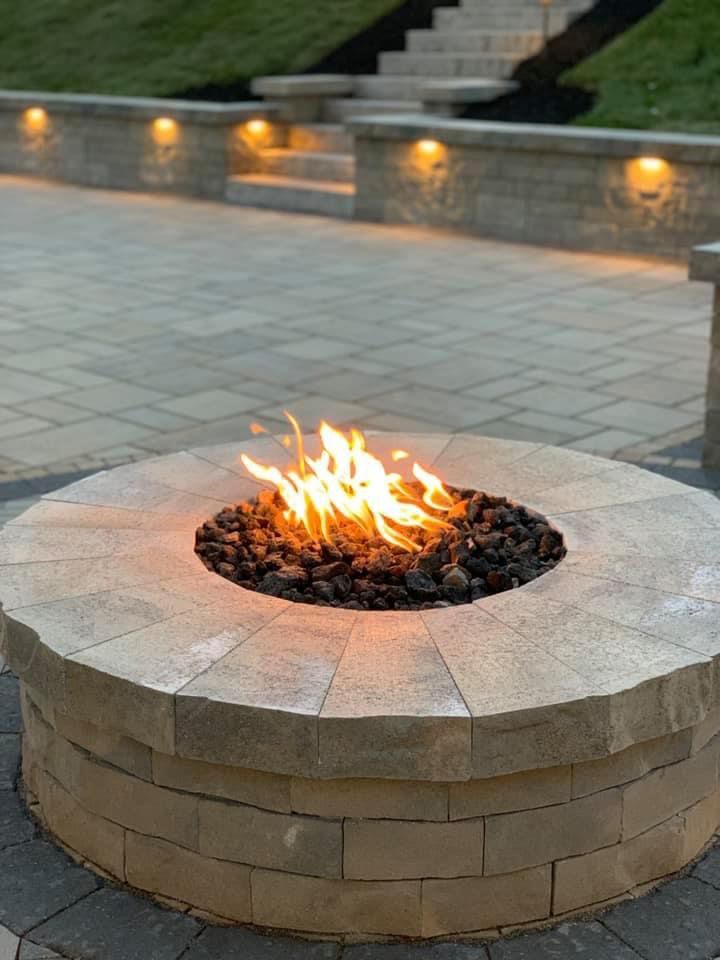A fire pit is lit up on a patio with stairs in the background.