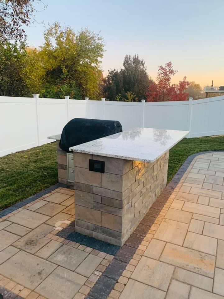 A brick island with a grill on top of it in a backyard.