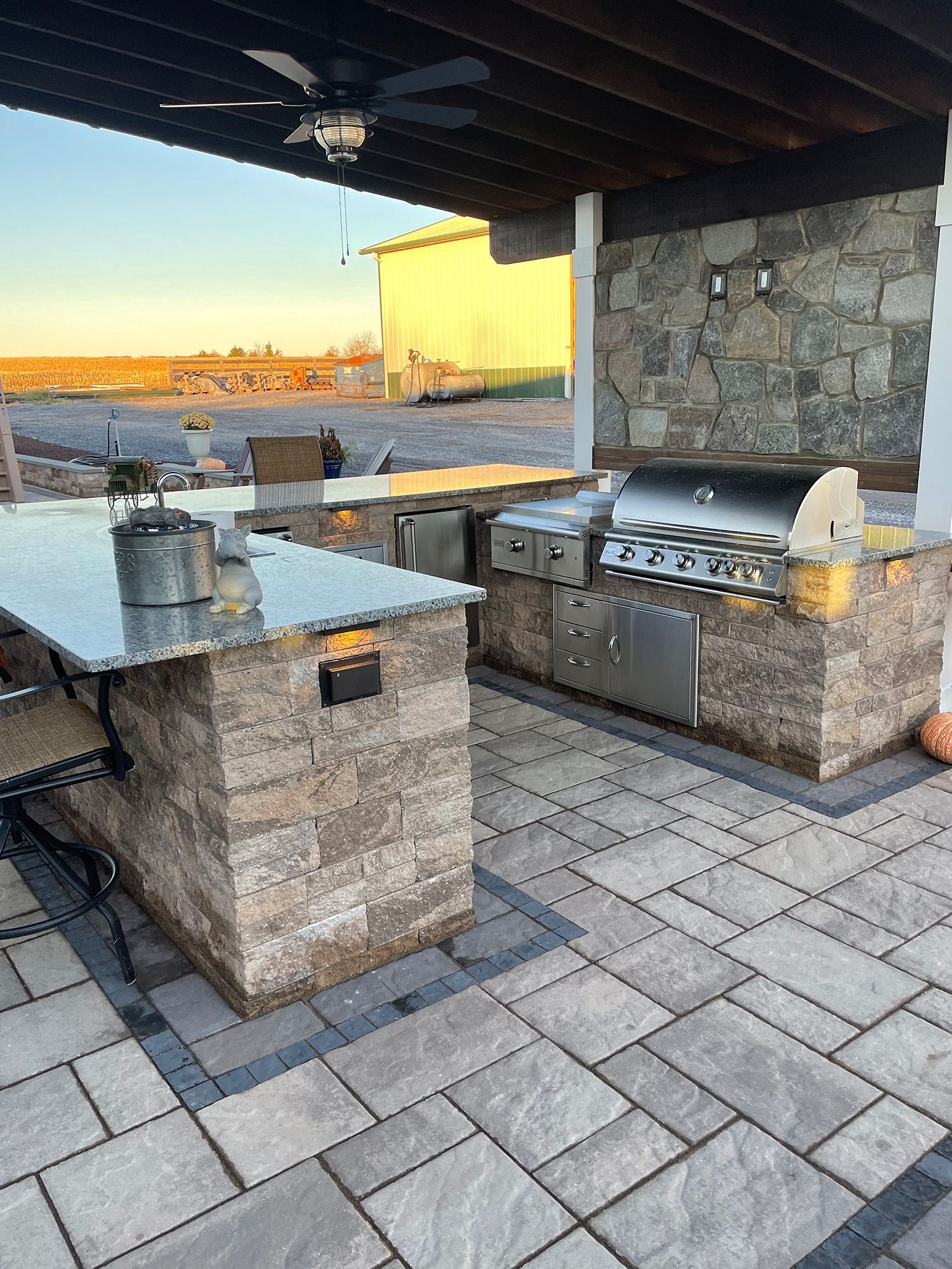 An outdoor kitchen with a grill and a table under a ceiling fan.