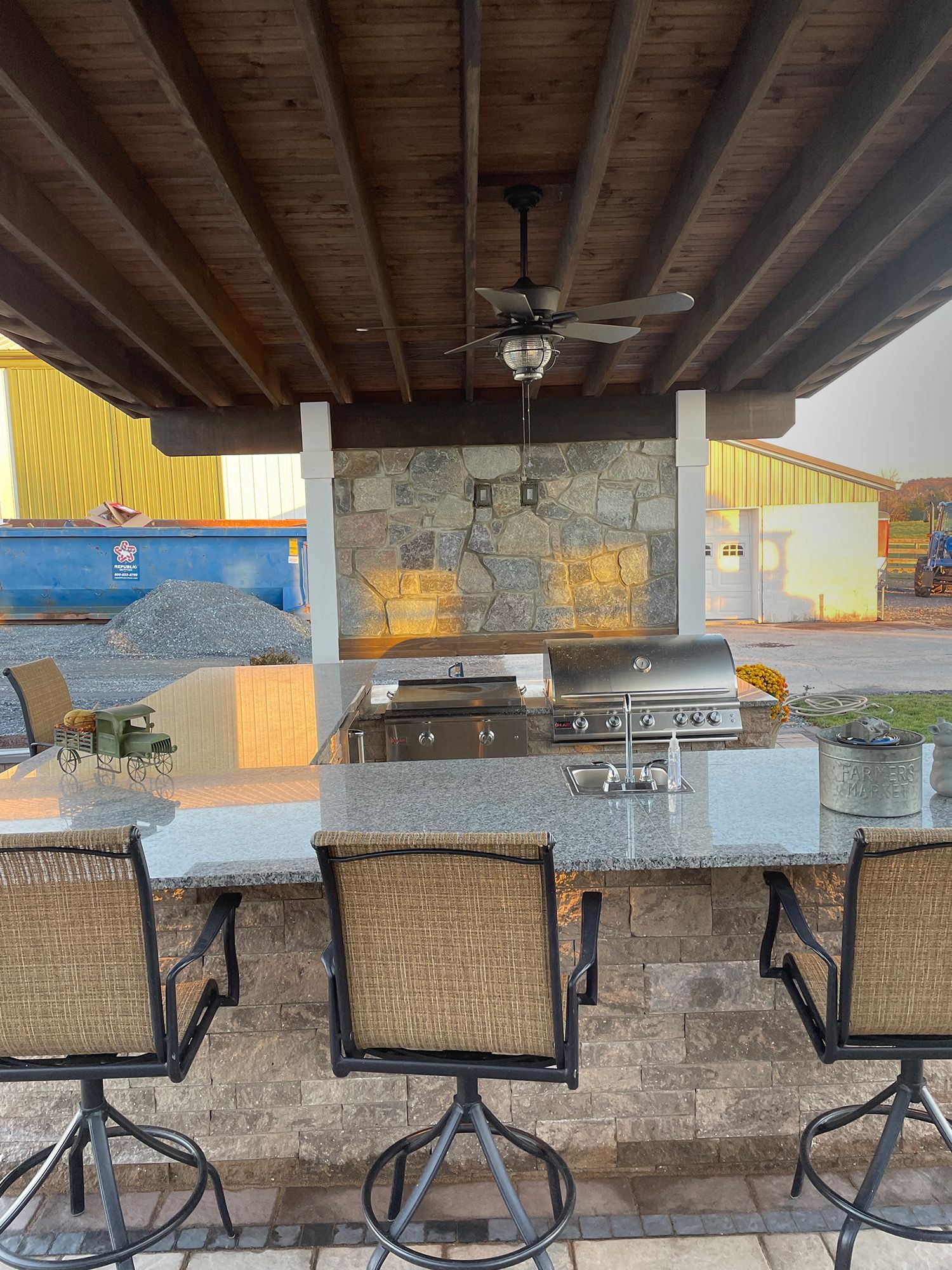 A patio area with a table , chairs , a grill and a ceiling fan.