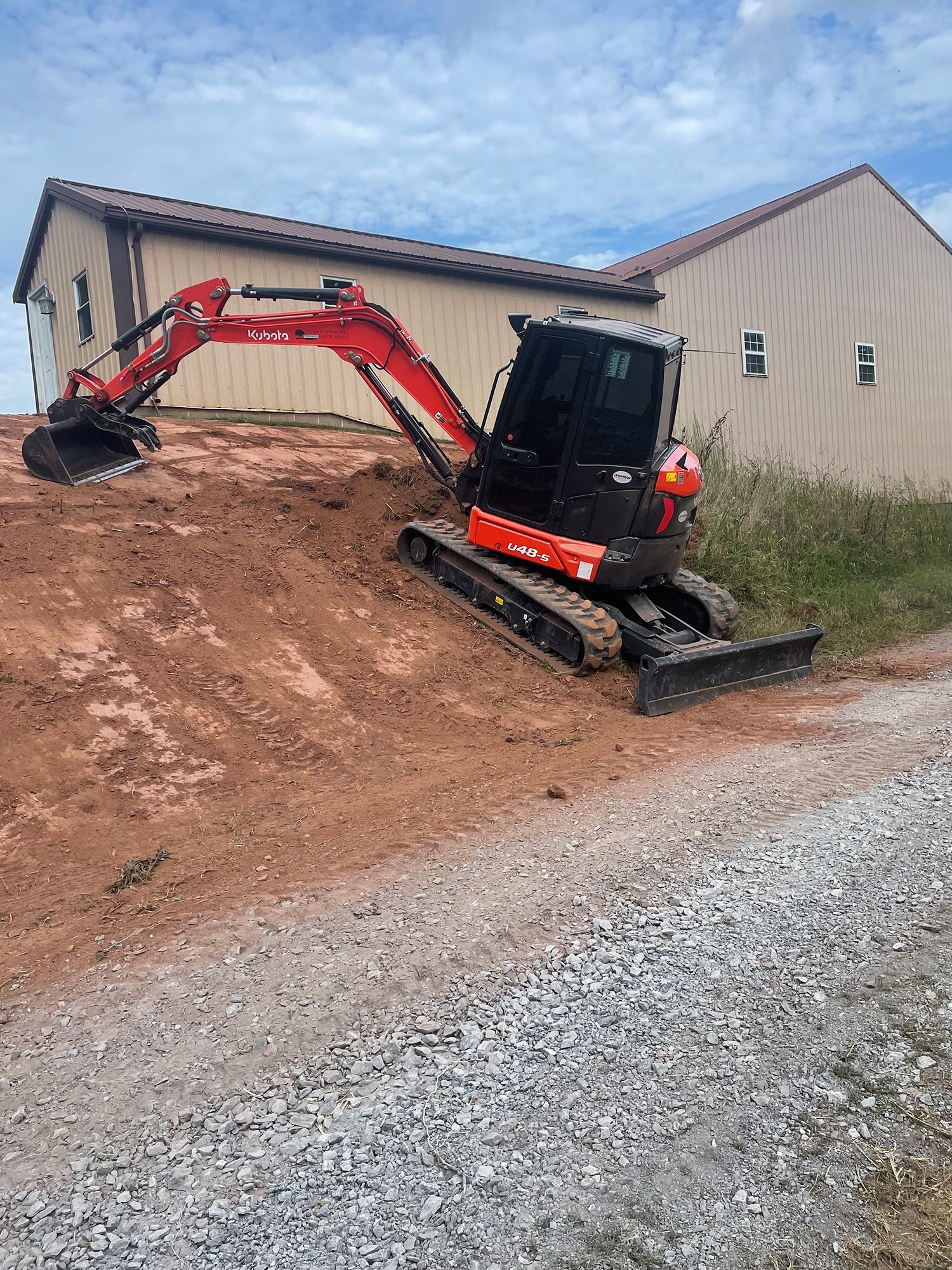 A small excavator is digging a hole in the dirt in front of a house.