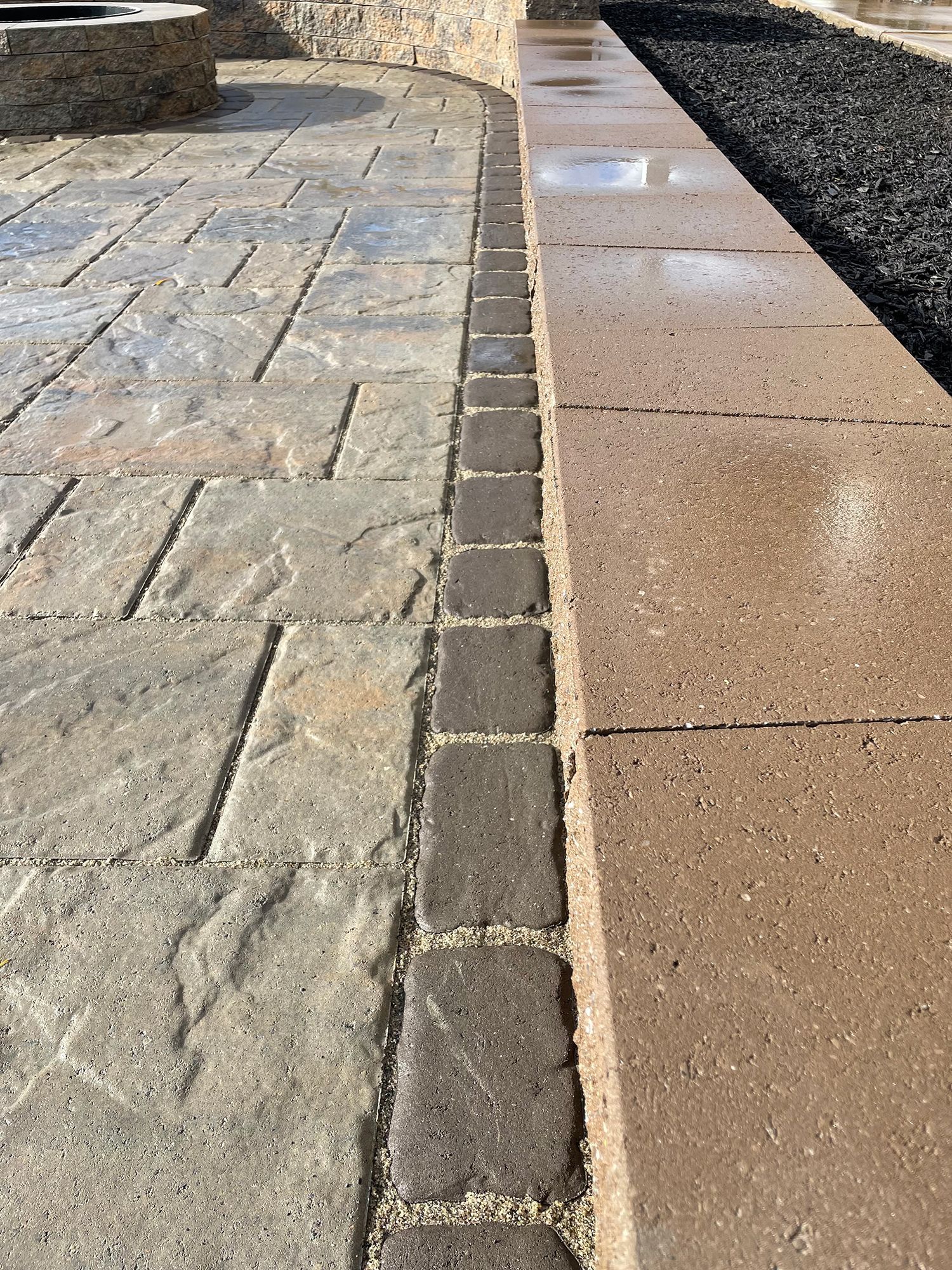 A close up of a brick walkway with a fire pit in the background.
