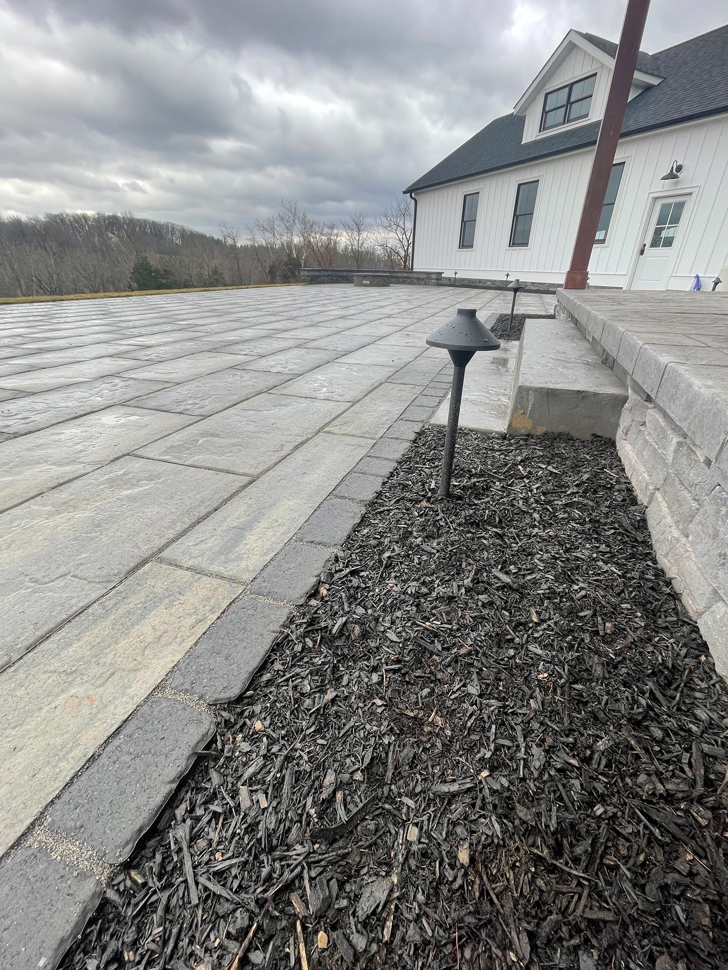A brick walkway with a light on the side of it in front of a house.
