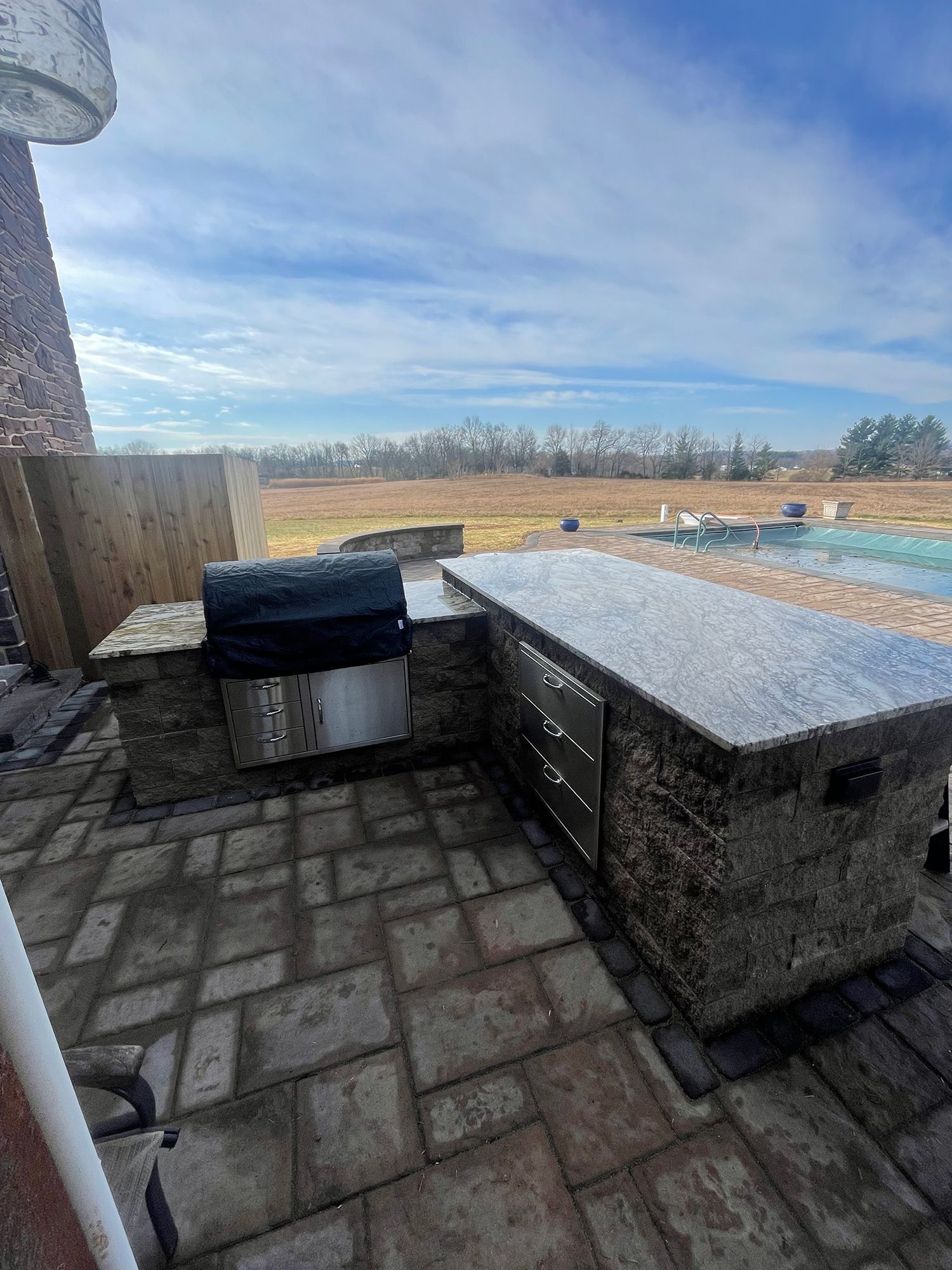 A patio with a grill and a swimming pool in the background.