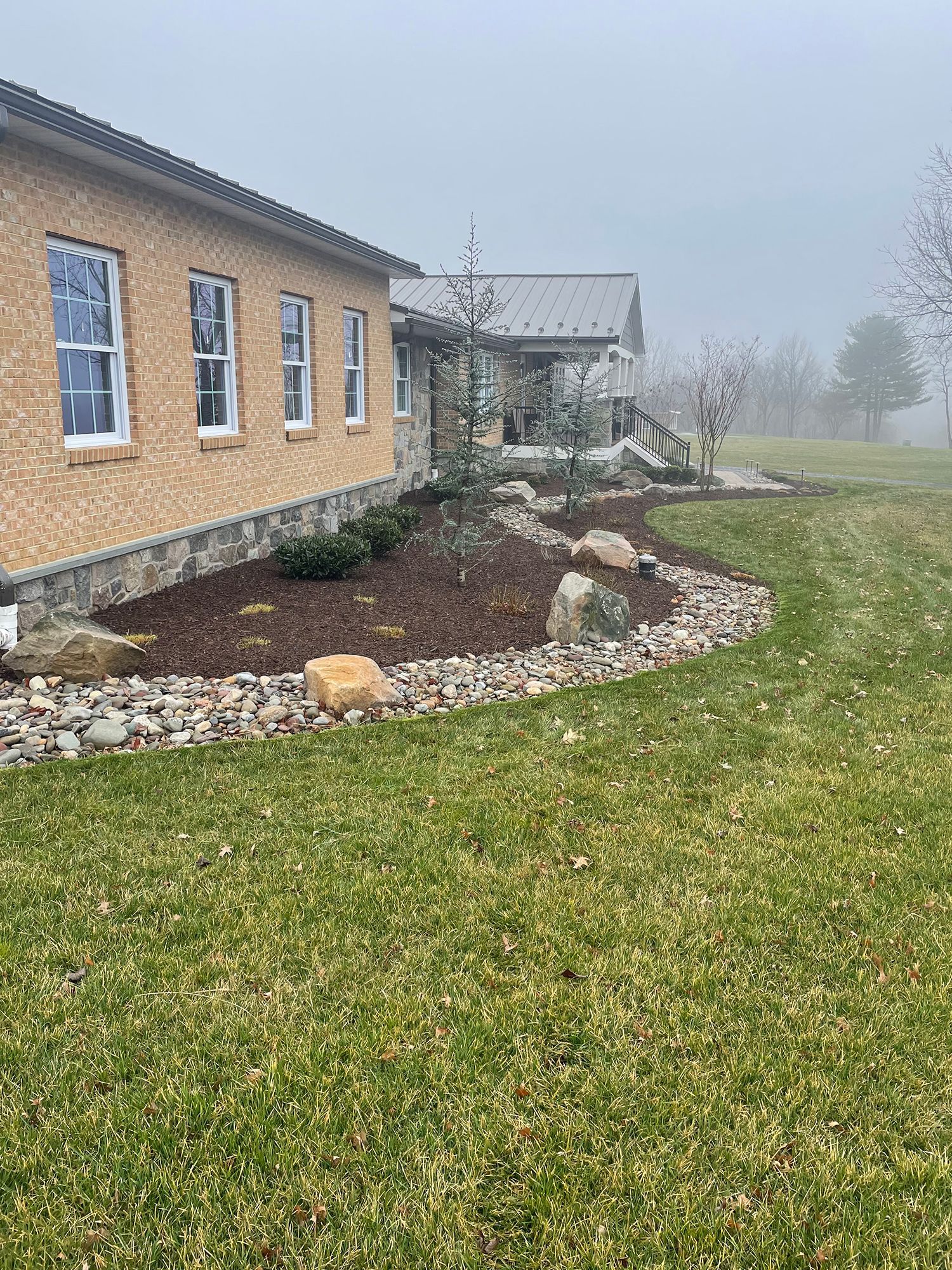 A brick house with a large lawn in front of it on a foggy day.