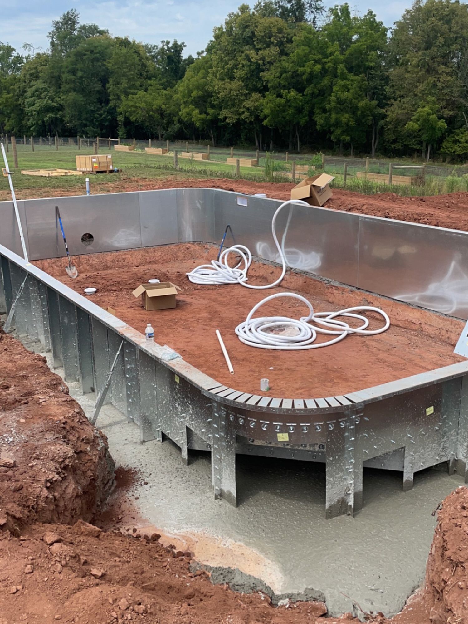A metal swimming pool is being built in a dirt field.